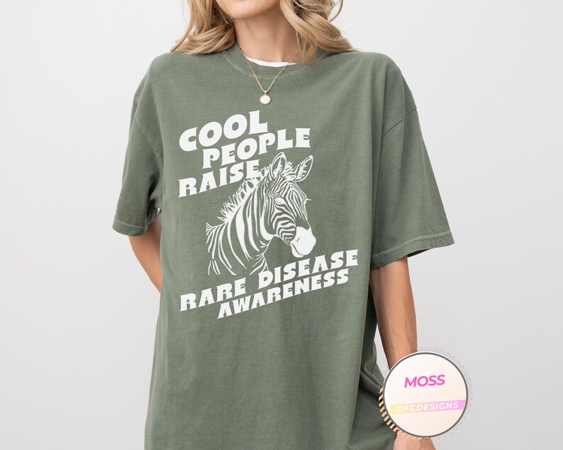 K&ouml;nnte beinhalten: Gr&uuml;nes T-Shirt mit wei&szlig;em Text, der "Cool People Raise Rare Disease Awareness" lautet, und einer Zebragrafik.