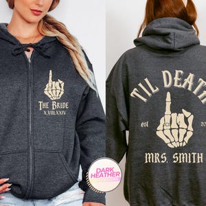 Puede incluir: Sudadera con capucha y cremallera gris oscuro con dise&ntilde;o de mano de esqueleto. En la parte delantera se lee "THE BRIDE" con n&uacute;meros romanos. La parte trasera dice "TIL DEATH" con "MRS. SMITH" y el a&ntilde;o 2024. Ropa tem&aacute;tica de boda.