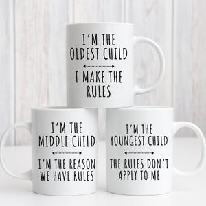 May include: Three white ceramic mugs with black text. The first mug says "I'm the oldest child I make the rules". The second mug says "I'm the middle child I'm the reason we have rules". The third mug says "I'm the youngest child the rules don't apply to me".