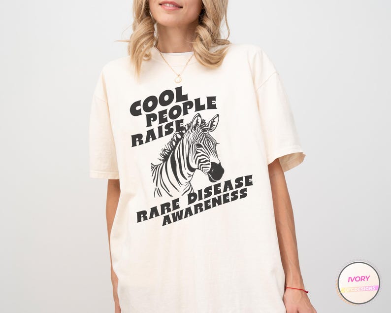 K&ouml;nnte beinhalten: Ein wei&szlig;es T-Shirt mit schwarzem Text, der "Cool People Raise Rare Disease Awareness" lautet, und einer Illustration eines schwarz-wei&szlig;en Zebras.