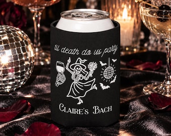 Könnte beinhalten: Ein schwarzer Dosenkühler aus Schaumstoff mit einer weißen Grafik eines Skeletts im Kleid, das ein Weinglas und einen Blumenstrauß hält, sowie einer Discokugel und Fledermäusen. Der Text lautet 'til death do us party' und 'CLAIRE'S BACH'.