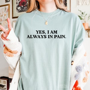 K&ouml;nnte beinhalten: Ein hellblaues T-Shirt mit dem Text "YES, I AM ALWAYS IN PAIN." in Schwarz gedruckt.