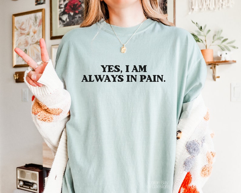 K&ouml;nnte beinhalten: Ein hellblaues T-Shirt mit dem Text "YES, I AM ALWAYS IN PAIN." in Schwarz gedruckt.