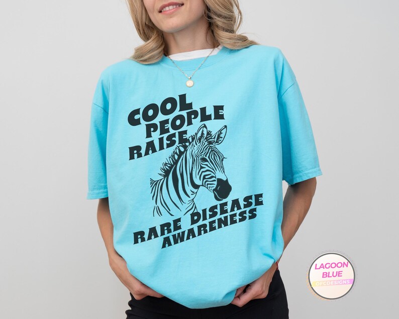 K&ouml;nnte beinhalten: Ein hellblaues T-Shirt mit einem schwarzen Zebra-Motiv und dem Text "Cool People Raise Rare Disease Awareness".