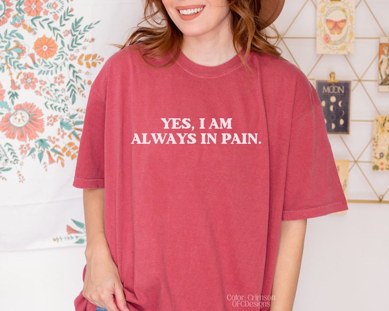 K&ouml;nnte beinhalten: Ein T-Shirt in einem kr&auml;ftigen Rotton mit dem in Wei&szlig; gedruckten Text "YES, I AM ALWAYS IN PAIN."
