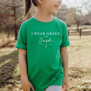 May include: A youth-sized Irish green t-shirt with the text "I WEAR GREEN for Josh" in white. The shirt also features a green ribbon graphic and the words "Cerebral Palsy Awareness".