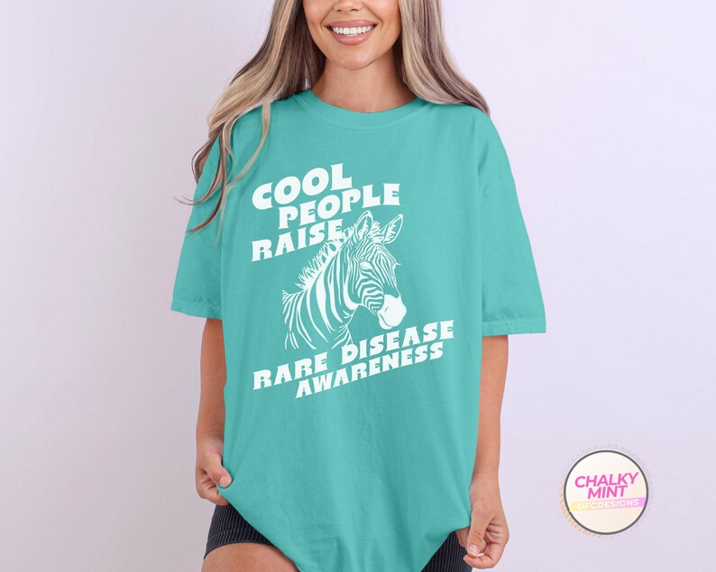 K&ouml;nnte beinhalten: T-Shirt in T&uuml;rkisblau mit einem wei&szlig;en Zebra-Motiv und dem Text "Cool People Raise Rare Disease Awareness."