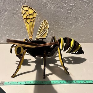 Può includere: Un modello di vespa in legno con strisce gialle e nere, ali marroni e occhi neri. Il modello è lungo circa 25 cm.