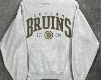 以下が含まれることがあります： ダークグレイのスウェットシャツ。前面に「BOSTON BRUINS」の文字がダークグリーンでヴィンテージ風にプリントされています。その下に「EST. B 1924」とBruinsのロゴ。木製のハンガーに掛けられています。