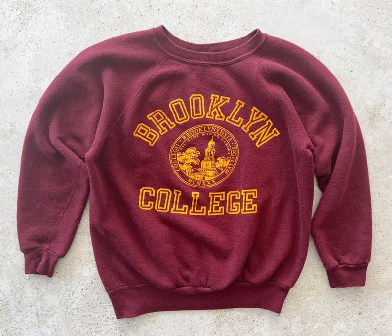 May include: A maroon sweatshirt with a yellow embroidered logo that says "Brooklyn College" and features a seal with a building and the words "Collegii Brooklynenis Sigillum MCMXXX"