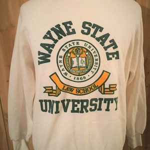 May include: White sweatshirt with a green and yellow Wayne State University Law School logo. The logo features a book, a torch, and the words "Wayne State University" and "Law School".
