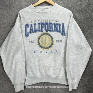 May include: Gray sweatshirt with the University of California Davis logo. The logo is blue and gold and features a book and a torch. The text "University of California" is in blue and the text "Davis" is in black.
