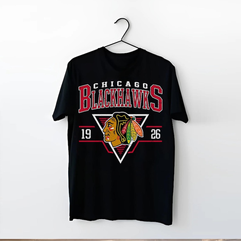 May include: Black t-shirt with a red, white, and black Chicago Blackhawks logo. The logo features a Native American headdress and the text "CHICAGO BLACKHAWKS" with the numbers "19" and "26" on either side.