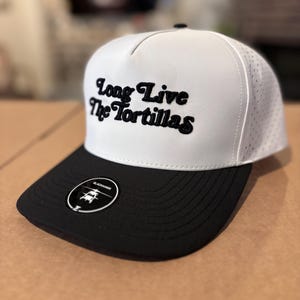 May include: A white and black baseball cap with the text "Long Live The Tortillas" in black script. The cap has a black brim and a small circular tag with a logo.