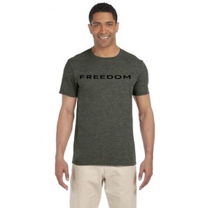 May include: A short-sleeved, olive green t-shirt with the word "FREEDOM" printed in black across the chest. The shirt is worn by a person, and paired with khaki pants. The person is smiling.