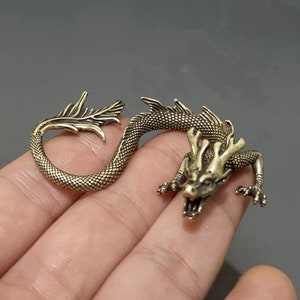 May include: A gold-coloured metal dragon figurine with a curled tail and detailed features. The dragon is posed with its head raised and mouth open, as if it is roaring.