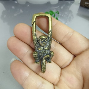 May include: A brass monkey keychain with a detailed design. The monkey is hanging from a metal ring, with its arms raised above its head. The keychain is a great way to add a touch of personality to your keys.