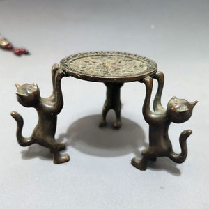 May include: A bronze decorative stand with a round top and three legs shaped like cats. The cats are holding up the top of the stand with their paws.