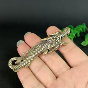 May include: A gold-toned dragon keychain with intricate details. The dragon is depicted with a long, scaly body and a fierce expression.