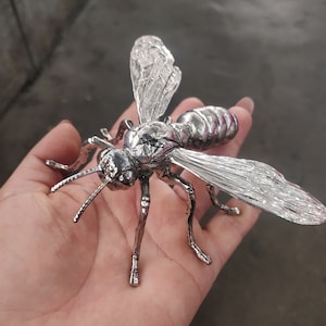 May include: A silver metal sculpture of a wasp with detailed wings and legs.