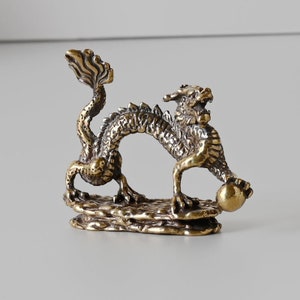 Peut inclure: Une petite figurine de dragon en métal doré tenant une perle. Le dragon est enroulé sur une base de roche.