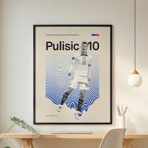 Pu&ograve; includere: Un poster incorniciato con Christian Pulisic in uniforme da calcio bianca con il numero 10. Il poster ha una cornice nera ed &egrave; esposto sopra una scrivania in legno. Lo sfondo presenta motivi a onde blu.