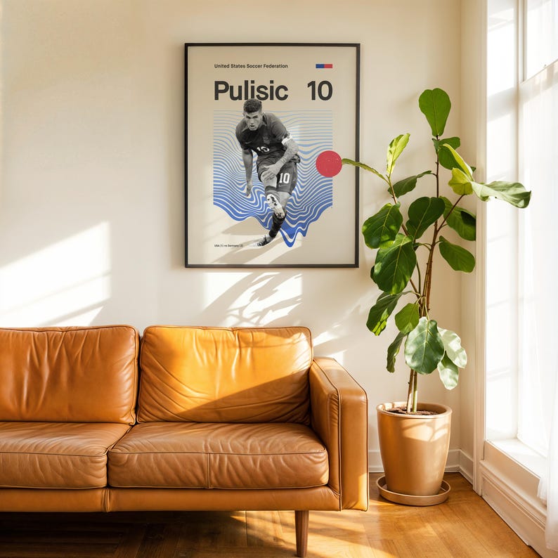 Pu&ograve; includere: Un poster incorniciato con il calciatore Pulisic, numero 10, su una parete bianca. Il poster ha una cornice nera. Un divano in pelle marrone e una pianta in vaso sono in primo piano. Il poster &egrave; in un salotto.