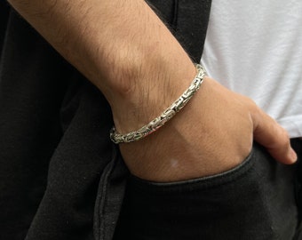 May include: A silver chain bracelet with a box chain design. The bracelet is worn on a person's wrist.