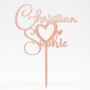 Peut inclure: D&eacute;coration de g&acirc;teau en or rose avec les noms "Christian" et "Sophie" en &eacute;criture cursive. Un c&oelig;ur est int&eacute;gr&eacute; au centre des noms. La d&eacute;coration est fix&eacute;e &agrave; une fine tige pointue pour &ecirc;tre ins&eacute;r&eacute;e dans un g&acirc;teau.