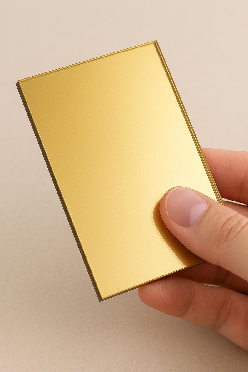 May include: A rectangular, gold-coloured object with a reflective surface. The object is held by a hand, showcasing its polished finish and metallic sheen. The edges are a darker shade of gold.