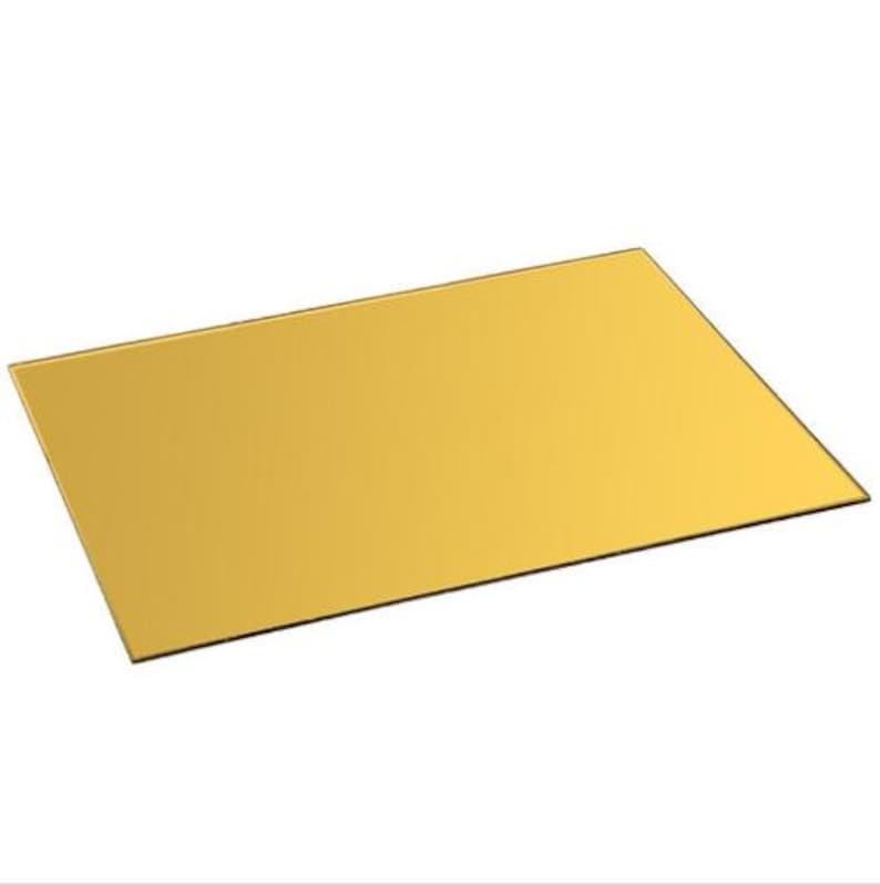 May include: A rectangular sheet of gold-coloured acrylic. The sheet has a smooth, reflective surface and is angled slightly, showcasing its shape and colour. The edges are clean and well-defined, suggesting a precision cut.