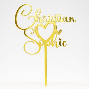 Peut inclure: Un cake topper dor&eacute; avec les noms "Christian" et "Sophie" &eacute;crits en cursive. Le design comprend un c&oelig;ur avec une fl&egrave;che et une tige pour l'insertion dans le g&acirc;teau. Le topper est fait d'un mat&eacute;riau r&eacute;fl&eacute;chissant.