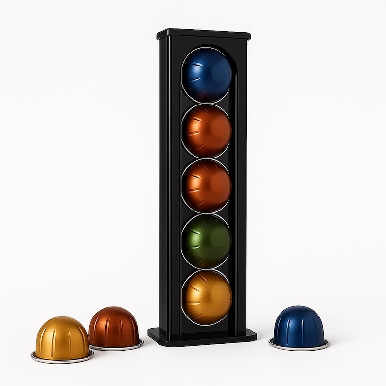 Op de afbeelding: Een zwarte koffiecapsulehouder met vijf kleurrijke capsules in blauw, oranje, bruin, groen en goud. Drie losse capsules in goud, bruin en blauw liggen aan de basis. De houder is voor koffiecapsules.
