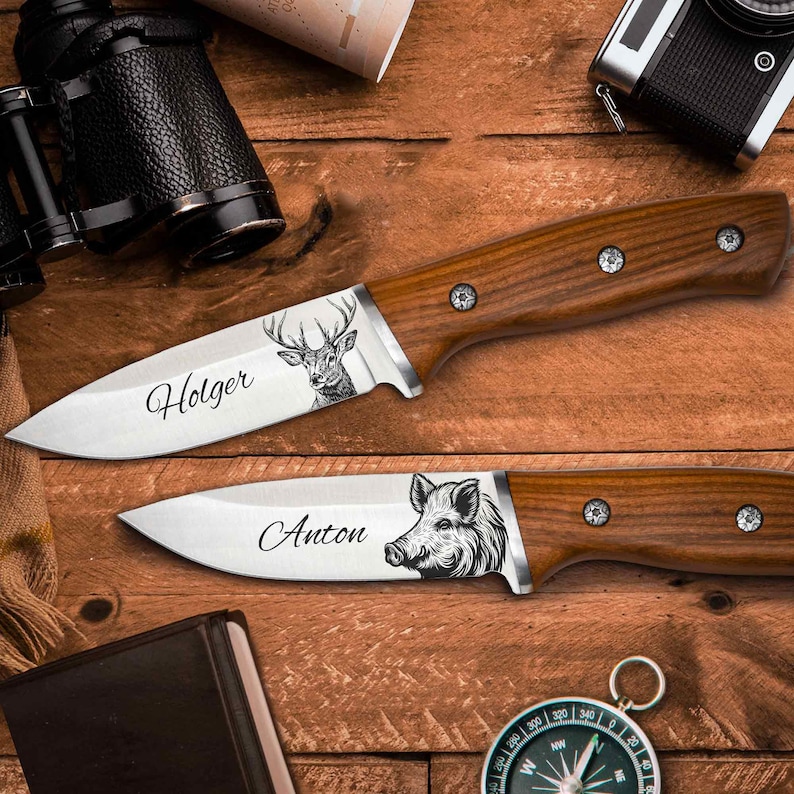 Ein Jagdmesser mit Gravur liegt auf einem Tisch neben einem Fernglas, einem Kompass und einem Buch mit Ledereinband.