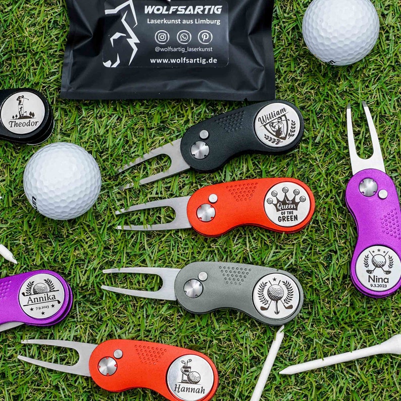Ein Golftool, bestehend aus einer Pitchgabel und einem Golfballmarker, der mittels Lasergravur personalisiert werden kann, präsentiert in verschiedenen Farben, auf einem Golfplatz. Die Golftools sind umgeben von Golfbällen und Tees.