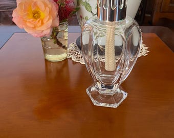 Könnte beinhalten: Eine klare Glas-Öllampe mit silbernem Oberteil und einem weißen Docht. Die Lampe steht auf einem Holztisch.