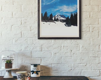 May include: A framed photograph of a snow-capped mountain peak with a blue sky and white clouds. The mountain is surrounded by trees and snow.