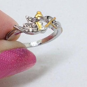 K&ouml;nnte beinhalten: Ein silberner Ring mit einem goldfarbenen Design eines Vogels mit Fl&uuml;geln und einer Krone auf dem Kopf. Der Vogel ist mit klaren Strasssteinen verziert.