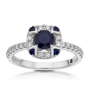 Puede incluir: Un anillo de plata con una piedra central de zafiro azul rodeada por un halo de diamantes más pequeños. La banda también está engastada con diamantes más pequeños.