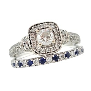 Puede incluir: Un anillo de compromiso de plata con un diamante central de forma cuadrada rodeado de diamantes más pequeños. La banda está adornada con diamantes más pequeños y una banda a juego con zafiros azules.