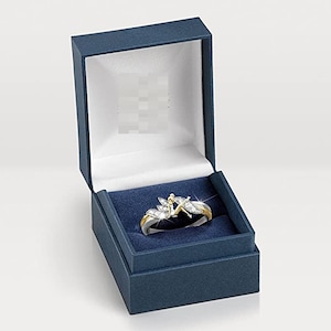 K&ouml;nnte beinhalten: Ein silberner Ring mit goldener Verzierung und einem klaren Kristalldesign mit einer Fee. Der Ring wird in einer blauen Samt-Ringbox pr&auml;sentiert.