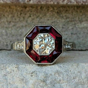 May include: A silver ring with a large, round, clear diamond surrounded by a octagon of red gemstones.