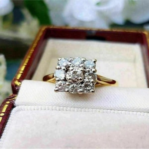 Op de afbeelding: Een gouden ring met een vierkante cluster van diamanten. De ring is gezet in een witgouden band en wordt gepresenteerd in een rode fluwelen ringdoos.