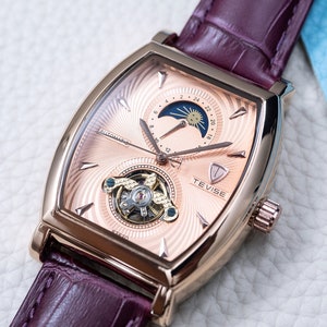 Peut inclure: Une montre-bracelet ton or rose avec un bracelet en cuir marron. Le cadran de la montre présente une complication de phase lunaire, un mouvement squeletté et le nom de la marque "TEVISE" imprimé sur le cadran.