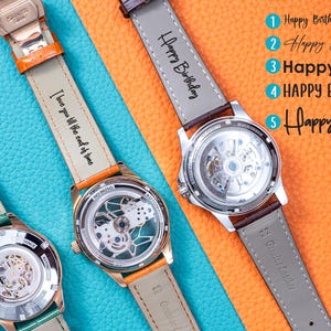 May include: Three automatic watches with visible internal mechanisms and leather straps. The straps are in various colors, including green, orange, and brown. Text on the straps includes "Happy Birthday" and "I love you till the end of time."