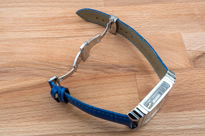 May include: A blue leather watch strap with a silver buckle and a clear case back. The strap is attached to a silver watch case.