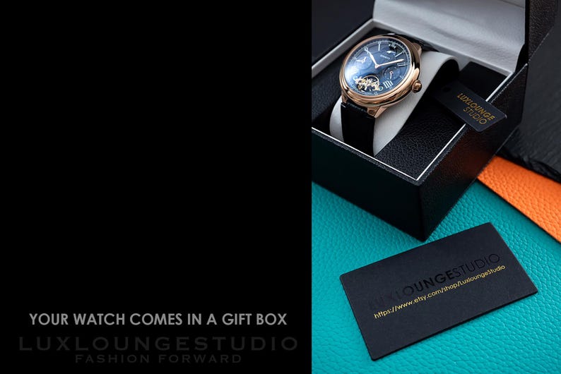 May include: A gold-toned wristwatch with a black leather band is displayed in a black gift box. The watch has a dark blue face and is presented on a white cushion. A black card with gold text reads "LUXLOUNGESTUDIO". The text "YOUR WATCH COMES IN A GIFT BOX" is also visible.