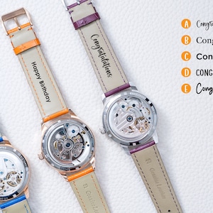 May include: Three wristwatches with different colored leather bands and personalized engravings. The bands are orange, purple, and blue. The engravings read "Happy Birthday", "Congratulations", and "I love you till the end of time".