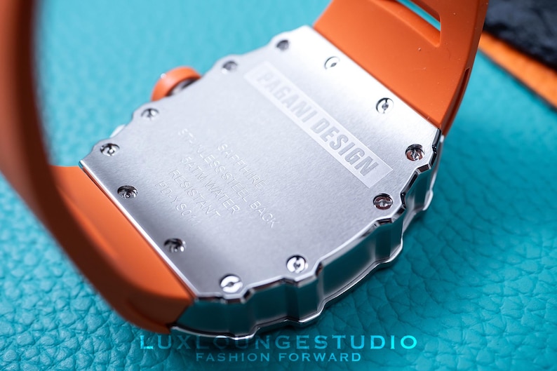 Peut inclure: Gros plan d'une montre Pagani Design. La montre a un dos argent&eacute; avec le nom de la marque et les sp&eacute;cifications. Elle est dot&eacute;e d'un bracelet en silicone orange. La montre est sur une surface turquoise.