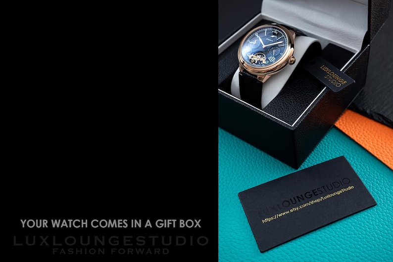 Puede incluir: Una caja de regalo negra con un reloj dorado en su interior. El reloj tiene una esfera azul con agujas doradas y n&uacute;meros romanos. El reloj est&aacute; en una correa de cuero negra. La caja est&aacute; sobre una superficie turquesa con una tarjeta de visita negra que dice "LuxLoungeStudio" y una direcci&oacute;n de sitio web.